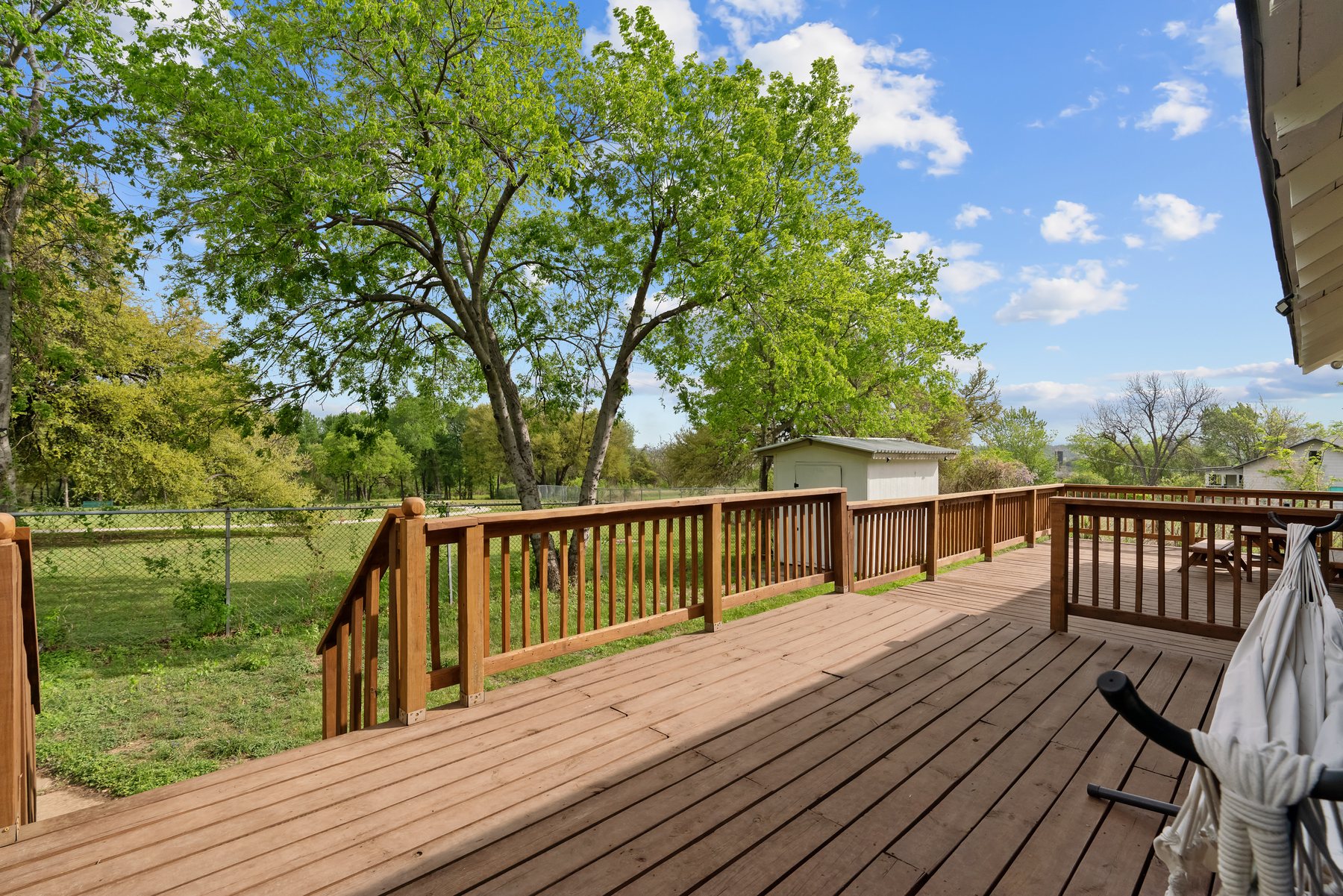 The rear deck of the house looking out over open lawn with mature trees beyond the back fence.